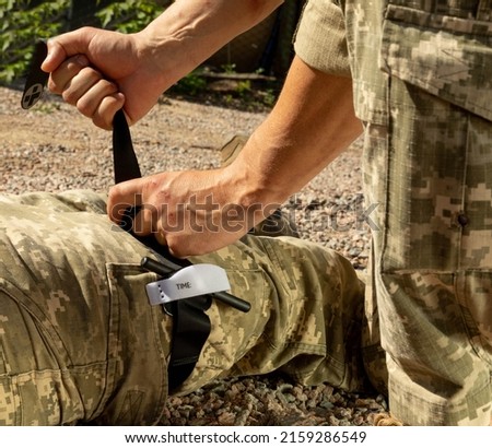Army medics practice applying a tourniquet to the leg of a wounded soldier. Combat tactical equipment. Combat use Turnstile. The concept of military medicine. Royalty-Free Stock Photo #2159286549