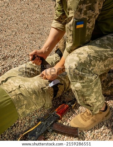 Army medics practice applying a tourniquet to the leg of a wounded soldier. Combat tactical equipment. Combat use Turnstile. The concept of military medicine. Royalty-Free Stock Photo #2159286551