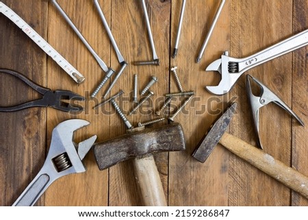 Top view of tools for DIY and repair work, DIY. Screws in the center of the picture surrounded by various tools such as screwdrivers, spanners, hammers on a wooden background.