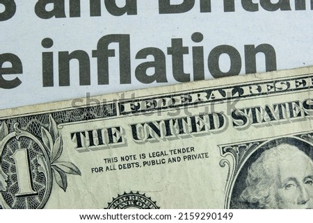 A US one dollar bill lying below a newspaper headline news on inflation. Concept for the dollar buying power amidst rising goods prices due to shortages and increasing demand. Closeup macro view. Royalty-Free Stock Photo #2159290149
