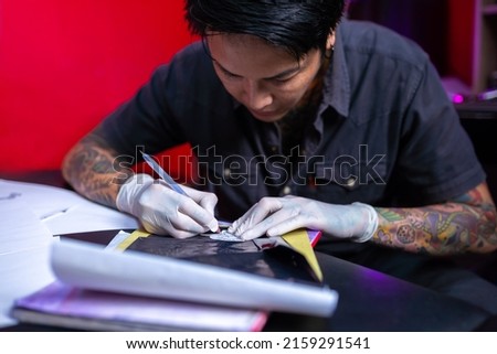 Preparing tattoo sketches. Professional tattoo master man paints sketches on paper to the customer. Selective focus sketches