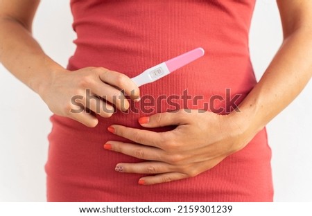 young woman showing a positive pregnancy test result and her pregnant belly in a pink tight dress