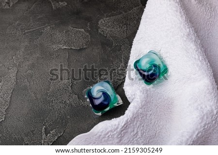 Laundry capsules and a snow-white towel on a black marble background. Laundry detergent for washing clothes in a washing machine. The concept of purity. Place for text.