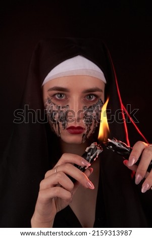 Portrait of a young creepy gothic girl making fire using two candles. Caucasian woman with creepy make-up. Satanic wicca religion concept.
