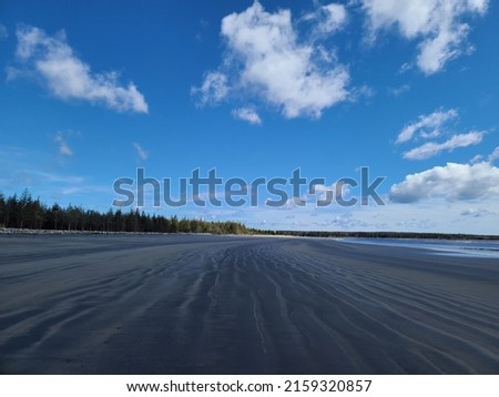 A long shot of a beach with few clouds in the blue sky above.