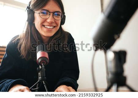 Handsome woman host streaming her audio podcast using microphone at small broadcast studio