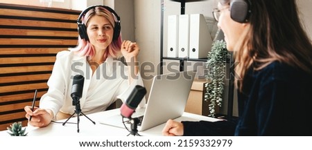 Two women streaming audio podcast using microphone and laptop at home broadcast studio