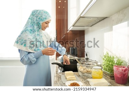 Muslim young woman in hijab cooking food in kitchen Royalty-Free Stock Photo #2159334947