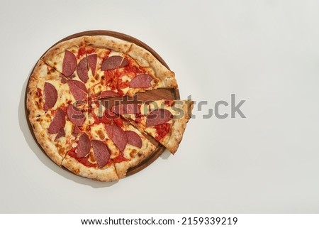 Top view of pepperoni pizza with one cut slice on circle wooden board. Unhealthy eating and fast food. Fresh baked delicious and appetizing junk food. White background in studio. Copy space