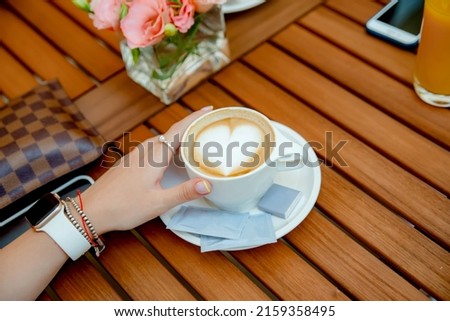 White hot coffee cup with steam on the table in blurred cafe background. Photo select focus. Closeup image of a woman hand