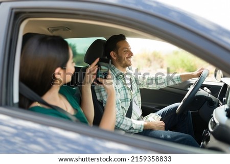 Young woman taking a picture of his cheerful boyfriend while driving for a fun vacation trip 