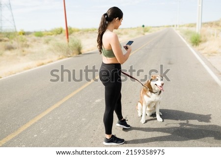 Rear view of a fitness young woman taking a picture of her adorable husky dog while working out outdoors 