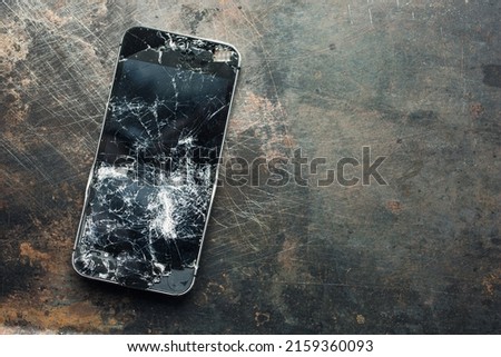 Badly damaged smartphone with bent metal case and broken glass on grunge background. Close-up.