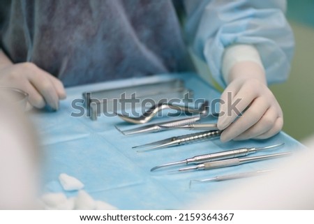 Surgical instruments in the operating room. A nurse in a surgical suit and gloves is preparing for a tooth implant operation.
Dental probe, tweezers, scalpel, needle holder, rasps on instrument table. Royalty-Free Stock Photo #2159364367