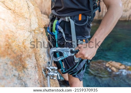 Climbing grips details young man's hand on rocks over the sea with rope and helmet.