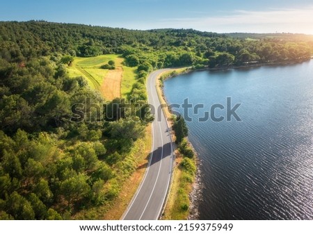 Aerial view of road near blue sea, forest at sunset in summer. Travel in Croatia. Top view of beautiful road, green trees, hills in spring. Colorful landscape with highway and sea coast. Road trip	
