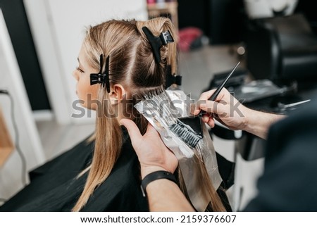 Hairdresser is applying bleaching powder on woman's hair and wrapping into the foil.  Royalty-Free Stock Photo #2159376607