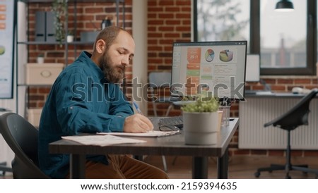 Employee analyzing rate charts on monitor and taking notes in startup office. Entrepreneur working on project planning and presentation to design business strategy and development.