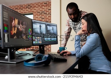 Post production house employee talking with coworker about footage quality. Professional movie editor sitting at desk while improving film frames using advanced specialized software.
