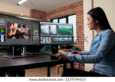 Asian professional video editor sitting at multi monitor workspace while enhancing movie footage quality using advanced software. Post production house team leader editing film frames.