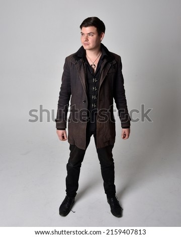 Full length portrait of  handsome brunette male model wearing black leather coat and elegant vest. Standing Pose with gestural hands reaching out,  isolated on studio background.
