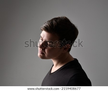 close up portrait of young brunette man in profile with silhouette rim lighting on studio background with a variety of canal expressions.