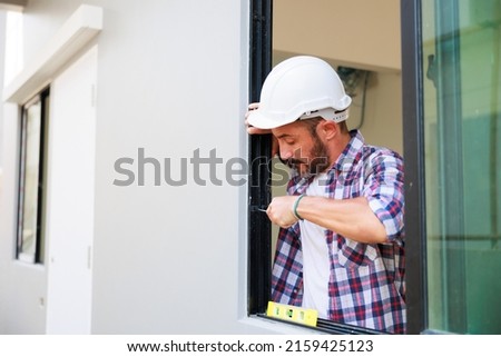 Man installing windows in  new house construction site. Hispanic Construction worker wearing protect gloves and hardhat helmet
