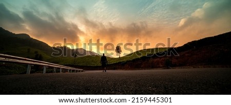 Panoramic view of wilderness scenic landscape in Munnar Kerala, Beautiful mountain sunset view and Young Photographer walking on wide road with camera	