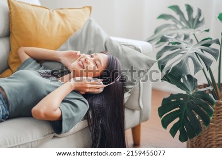 Happy woman relaxing in her sofa at home, Smiling girl is listening to music with headphones and lying down with eyes closed, Enjoy good quality sound, Stress free concept. Royalty-Free Stock Photo #2159455077