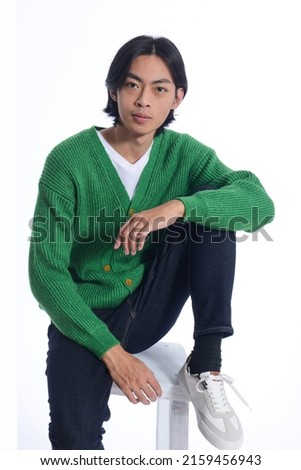 fashion model. Young man with hairstyle in green sweater sitting chair on white background


