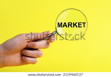Hand with magnifier with word market on yellow background. Conducting research about new product, service, customers satisfaction assessment. Marketing concept. High quality photo