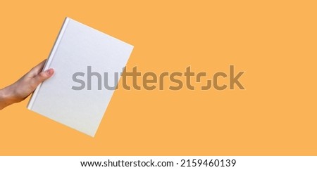 Banner with hand holding book mockup on orange background. Education, reading hobby, wisdom, intellectual development concept. Copy space. High quality photo Royalty-Free Stock Photo #2159460139