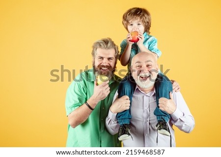 Grandfather father and son hugging and eating apple. Men in different ages, isolated on yellow. Royalty-Free Stock Photo #2159468587