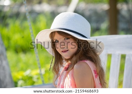 Charming cute caucasian little girl wearing straw hat standing outdoors. Funny kids face. Happy child relax in spring background.