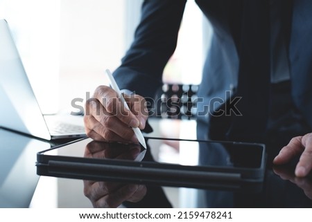 Businessman using stylus pen signing e-document on digital tablet with laptop computer on table at office, e-signing, electronic signature, paperless office concept