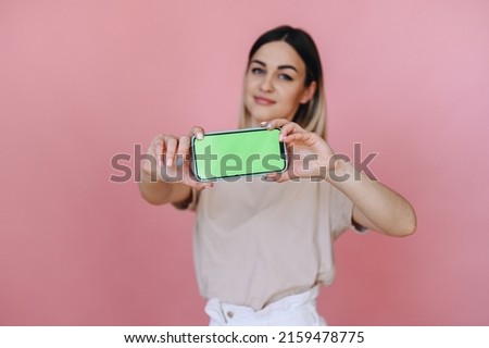 girl is holding horizontally a smart phone with a green screen on a pink background, focus on the phone. Place for advertising