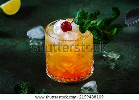 Mai Tai popular alcoholic cocktail with rum, liqueur, syrup, lime juice, mint and crushed ice. Dark green background, steel bar tools, negative space Royalty-Free Stock Photo #2159488109