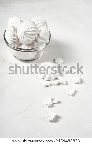glass vase with meringue stands on a gray background, next to it are a whole and broken dessert of French meringue, a vertical picture.