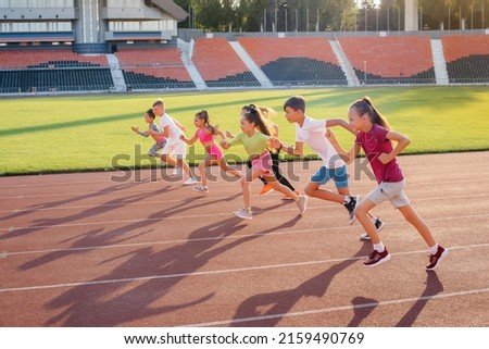 A large group of children, boys and girls, run and play sports at the stadium during sunset. A healthy lifestyle. Royalty-Free Stock Photo #2159490769
