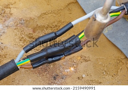 Heat-shrink tubing over underground cables is shrunk with a gas flame Royalty-Free Stock Photo #2159490991