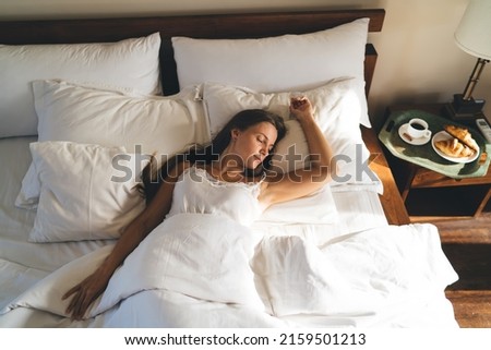 Young female 20 years old in comfy bedclothes watching sweet dreams enjoying sunday morning for long napping in hotel, Caucasian woman lying in cozy bedroom sleeping during lazy day on weekend Royalty-Free Stock Photo #2159501213