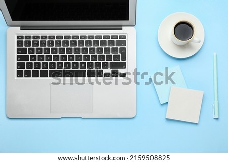 Blank sticky notes, pen, laptop and cup of coffee on blue background