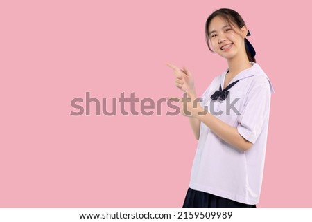Happy braces Asian student girl in school uniform finger pointing on isolated pastel background.