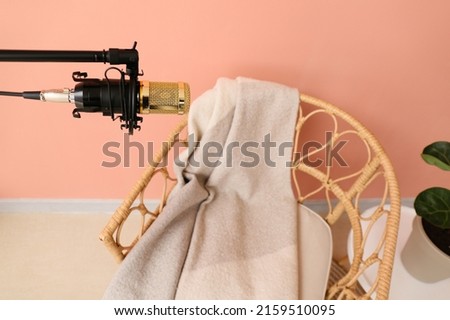 Stand with professional microphone and chair near color wall