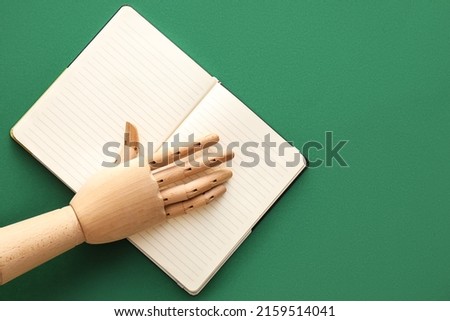 Wooden hand with notebook on green background