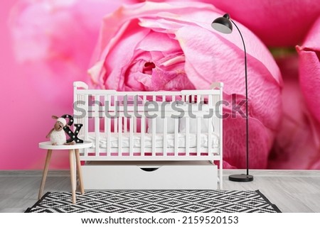 Baby bed with table and lamp near wall with printed beautiful pink flower on wall