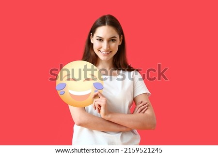 Pretty young woman holding emoticon with tears of joy on red background
