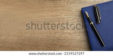 Beautiful fountain pen and blue notebook on wooden table, top view with space for text. Banner design