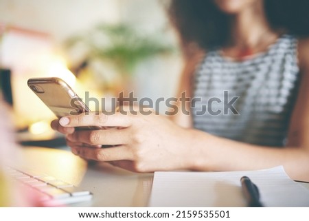 Shot of an unrecognizable young woman sitting alone and using her cellphone to work from home stock photo