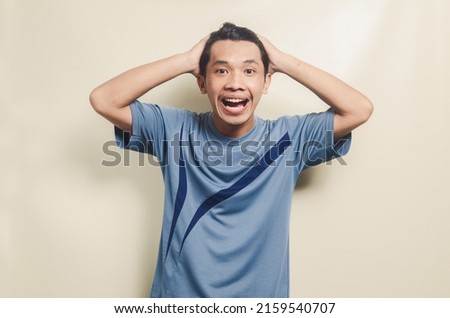 Asian young man in sports t-shirt looks shocked isolated on background